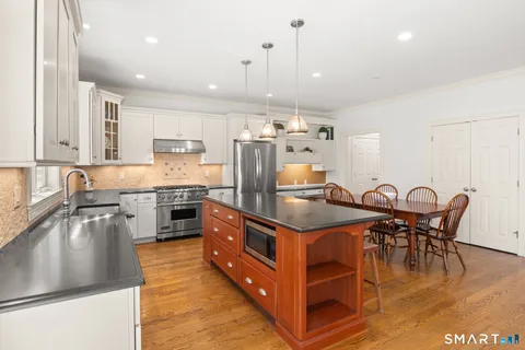 a kitchen with stainless steel appliances granite countertop a stove top oven a sink dishwasher a dining table and chairs with wooden floors