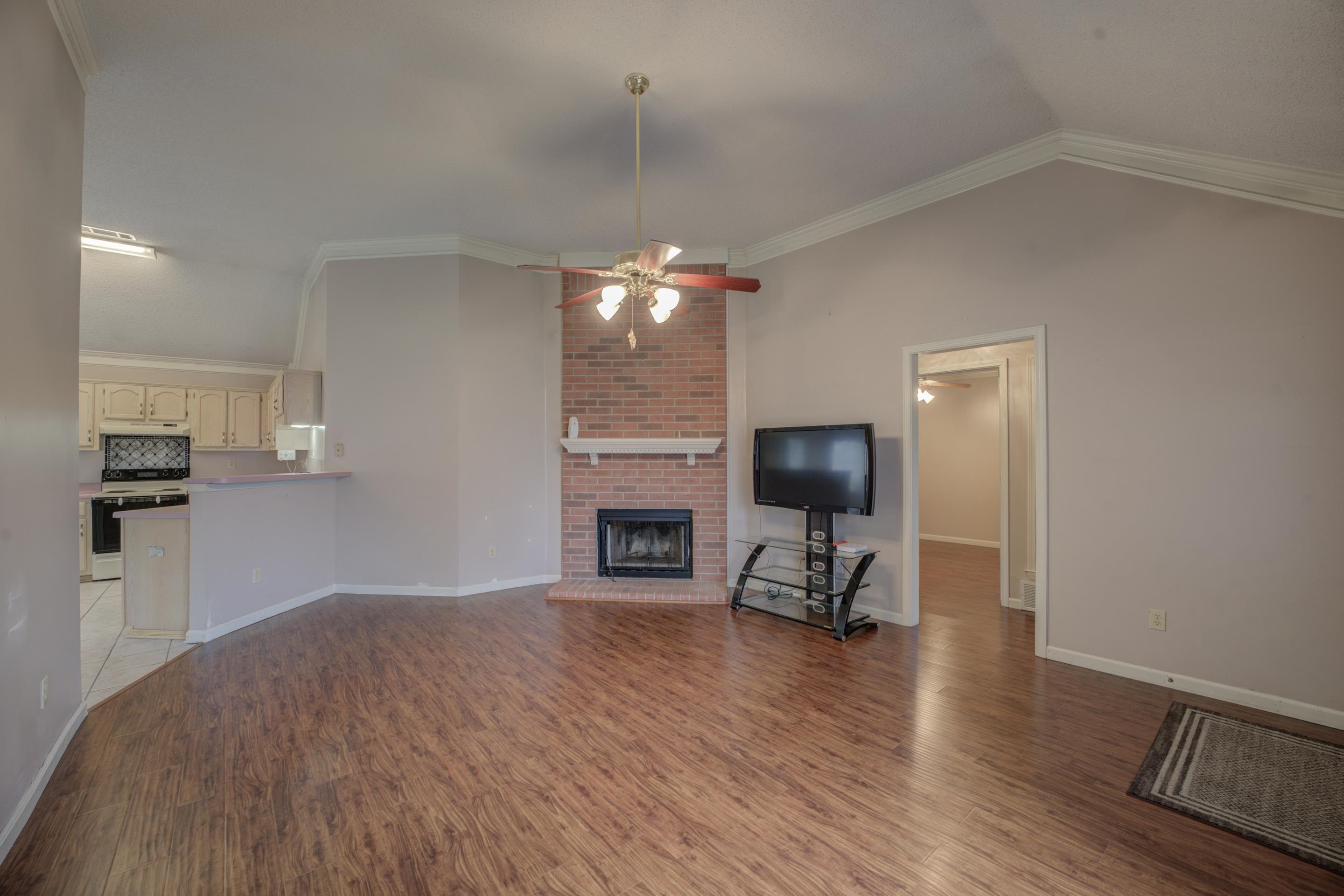 7657 Stone Manor Road Memphis, TN 38125 - Photo 6 of 27 Unfurnished living room featuring ornamental molding, ceiling fan, a fireplace, light wood-type flooring, and vaulted ceiling