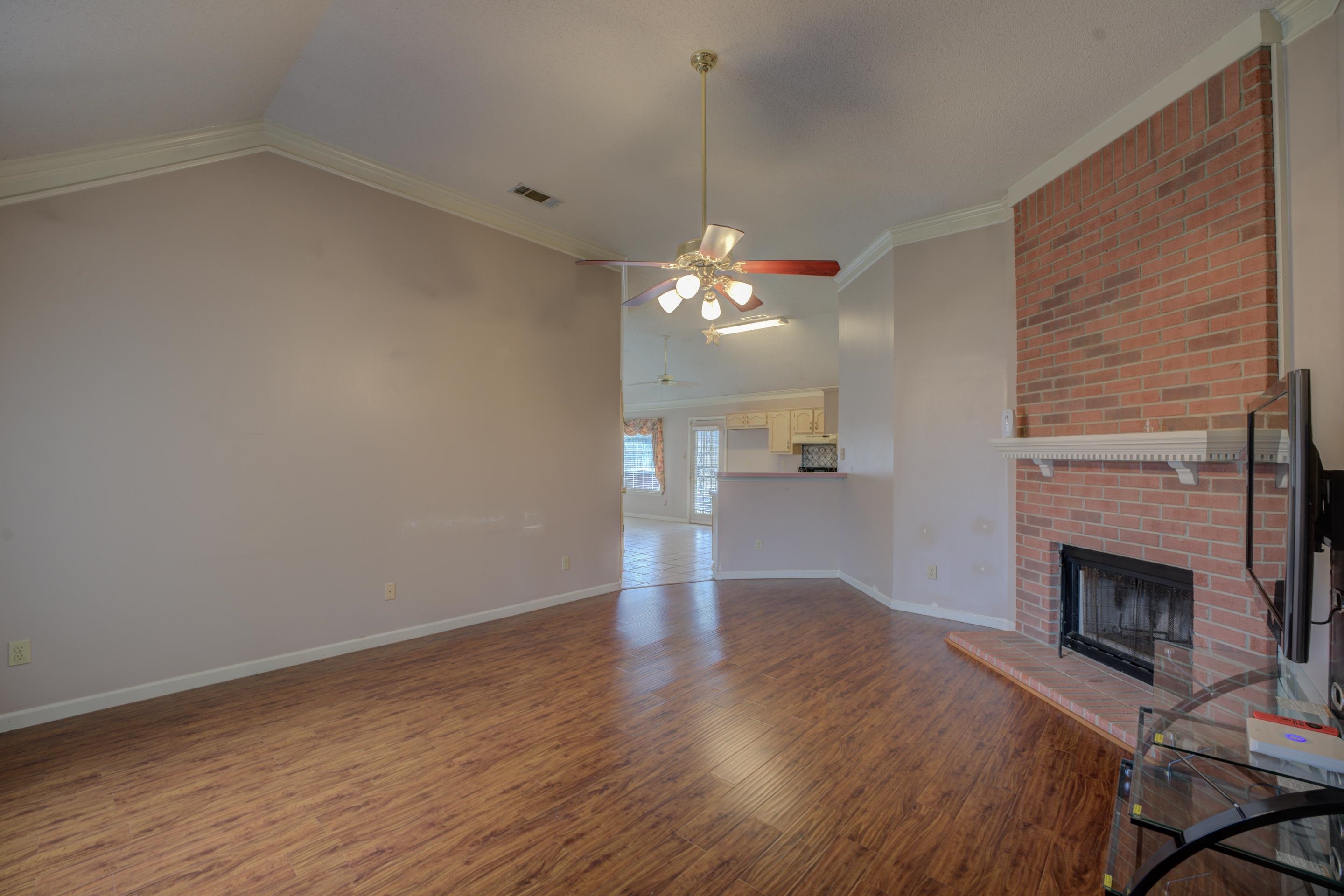 7657 Stone Manor Road Memphis, TN 38125 - Photo 7 of 27 Unfurnished living room with wood-type flooring, crown molding, vaulted ceiling, a brick fireplace, and ceiling fan