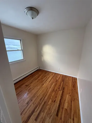 an empty room with wooden floor a exposed radiator and a window