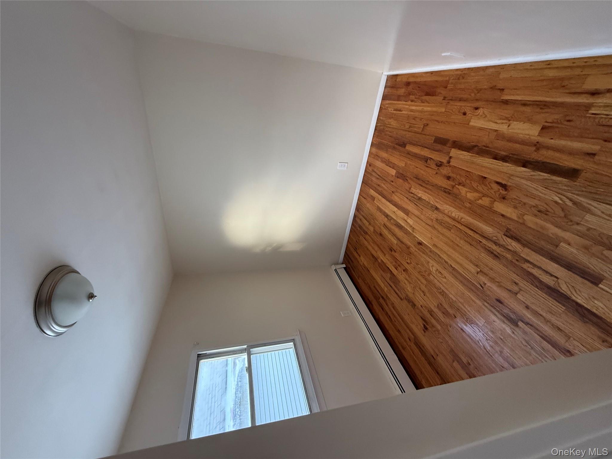 102-12 216th Street Queens, NY 11429 - Photo 5 of 10 an empty room with wooden floor a exposed radiator and a window