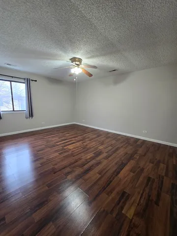 an empty room with wooden floor chandelier fan and windows