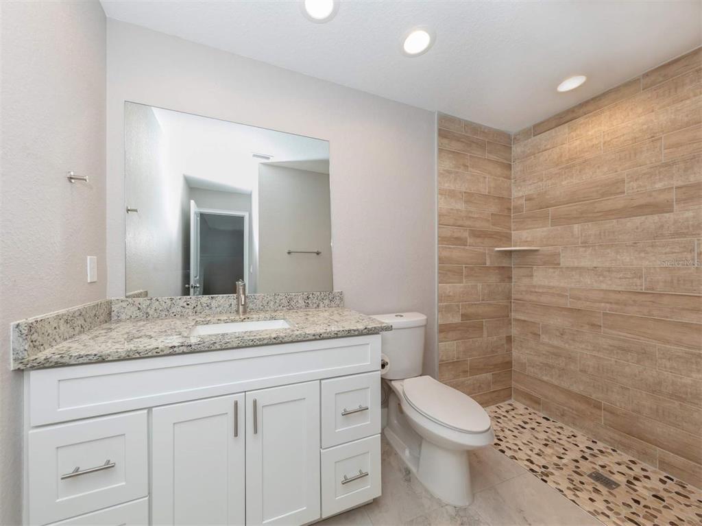 125 Boundary Boulevard, Unit 2 Rotonda West, FL 33947 - Photo 23 of 32 a bathroom with a granite countertop toilet a sink a mirror and shower
