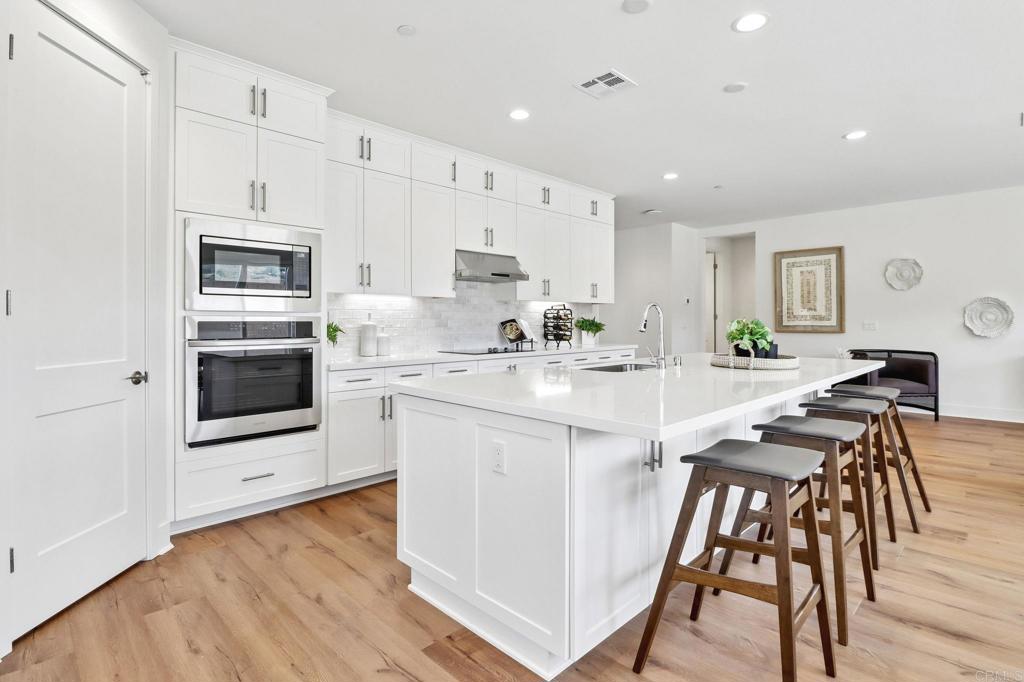 3521 Butler Place Escondido, CA 92027 - Photo 21 of 50 a kitchen with stainless steel appliances a stove a sink a microwave a refrigerator and white cabinets with wooden floor