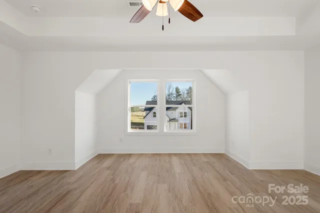 an empty room with wooden floor chandelier fan and windows