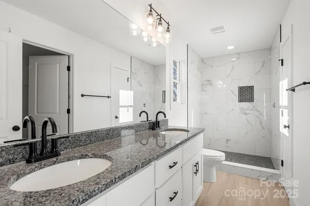 a bathroom with a granite countertop double vanity sink toilet and shower