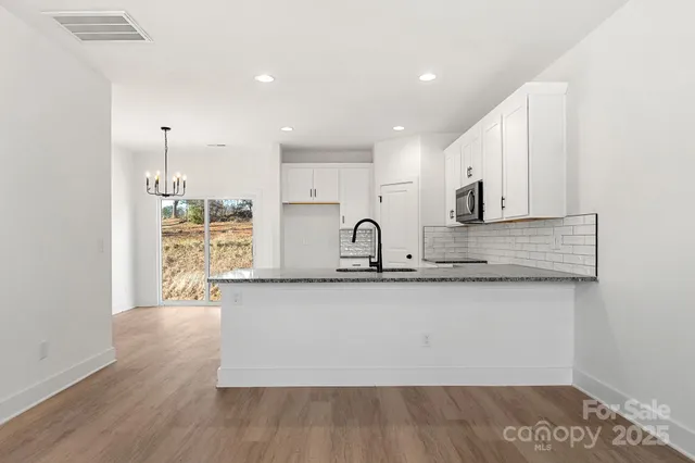 a large kitchen with granite countertop a stove a sink a refrigerator and white cabinets with wooden floor