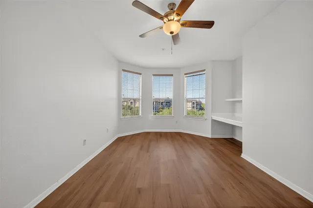an empty room with wooden floor chandelier fan and windows