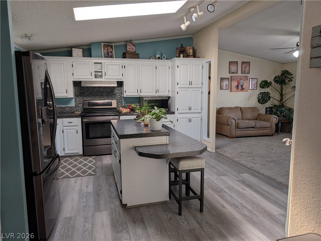 320 6th Street Panaca, NV 89042 - Photo 8 of 31 Kitchen with a breakfast bar area, white cabinetry, dark countertops, stainless steel appliances, and rail lighting