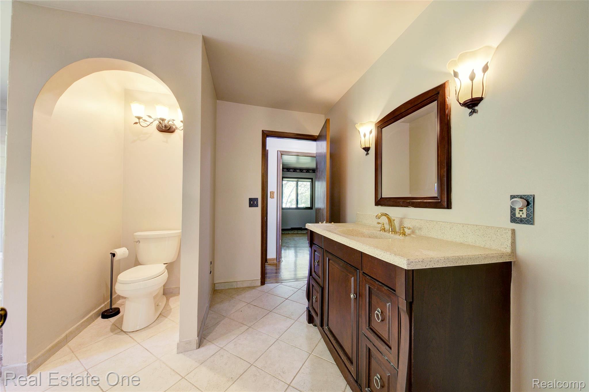 3125 West Commerce Road Milford, MI 48380 - Photo 28 of 63 Bathroom featuring a dual-sink vanity with a light-toned countertop, a wood-framed mirror, and two wall-mounted sconces
