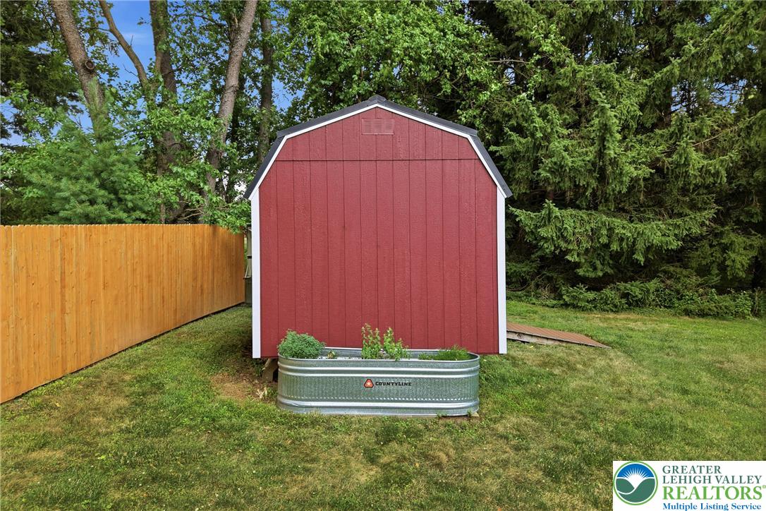 1553 Surrey Road Bethlehem, PA 18015 - Photo 80 of 92 A vibrant red shed with white trim stands prominently amidst a green lawn and mature trees, offering functional outdoor storage.