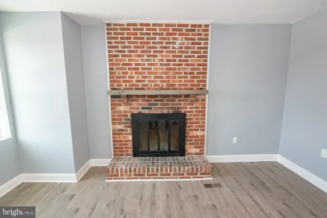 a view of an empty room with wooden floor and a fireplace