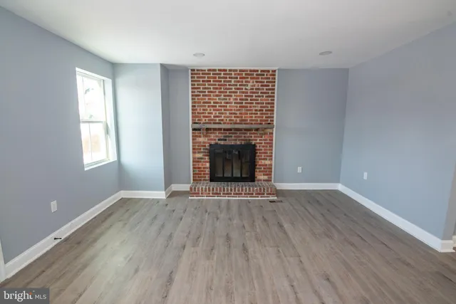 an empty room with wooden floor fireplace and windows