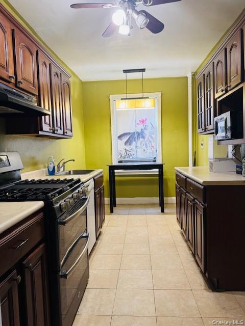 48-20 44th Street, Unit 4C Queens, NY 11377 - Photo 6 of 12 Kitchen featuring appliances with stainless steel finishes, dark brown cabinetry, light countertops, under cabinet range hood, and light tile patterned floors