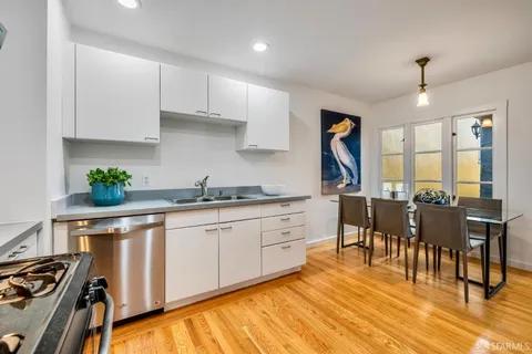 a open kitchen with stainless steel appliances granite countertop a stove top oven a sink a dining table and chairs with wooden floor