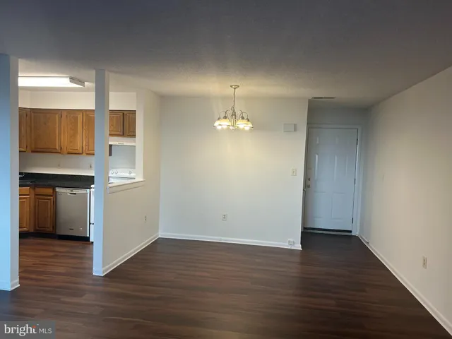a view of empty room with wooden floor and kitchen
