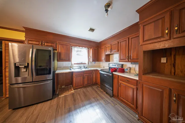 a kitchen with stainless steel appliances kitchen island granite countertop a refrigerator a sink dishwasher a stove and white countertops with wooden floor