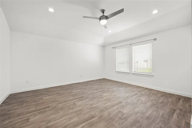 an empty room with wooden floor ceiling fan and windows