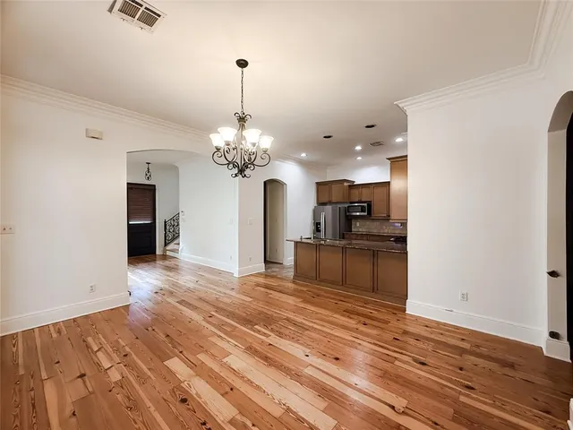 a view of an empty room and kitchen with wooden floor