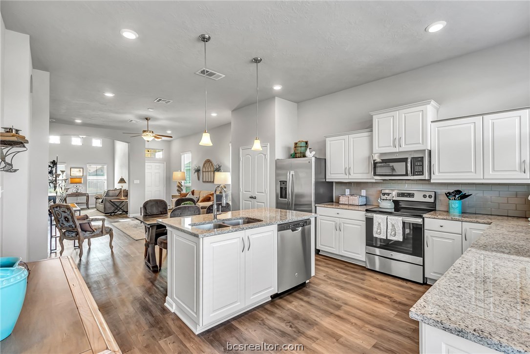 2103 Dumfries Drive Bryan, TX 77807 - Photo 1 of 1 a kitchen with stainless steel appliances kitchen island granite countertop a stove top oven a sink a refrigerator white cabinets and wooden floor