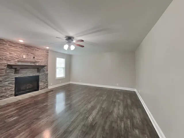 a view of an empty room with wooden floor fireplace and a window