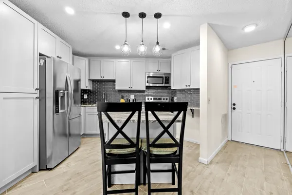 a kitchen with stainless steel appliances a dining table chairs refrigerator and microwave