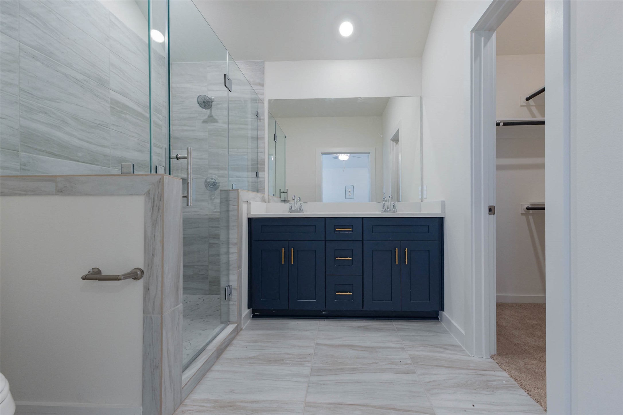 1115 Santee Court Rosharon, TX 77583 - Photo 14 of 23 The primary bath is an upgrade you will notice daily, with a long navy double vanity, white counters, gold drawer pulls and a frameless glass shower with wood-grain tile. A walk-in closet door sits at the far end, so you can move from shower to wardrobe without stepping into the bedroom. Bright lighting and a large mirror make it ideal for getting ready.