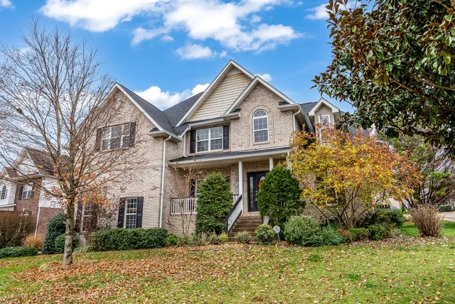 a view of a white house next to a yard with large trees