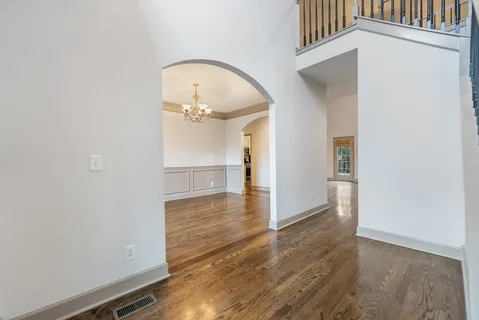 an empty room with wooden floor staircase and a kitchen view