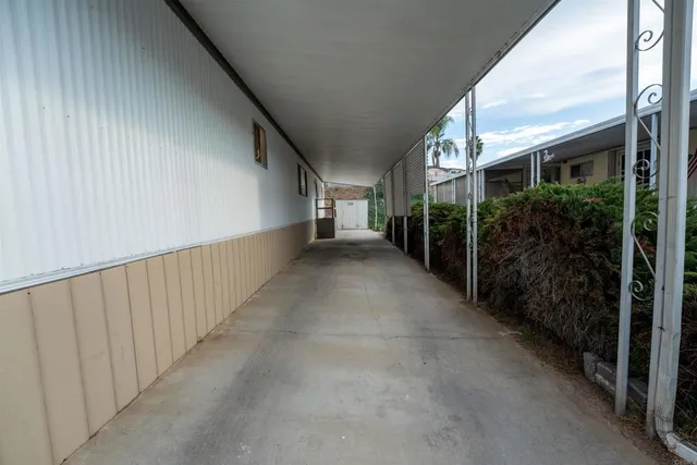 a view of a hallway to an empty room with wooden floor and a kitchen