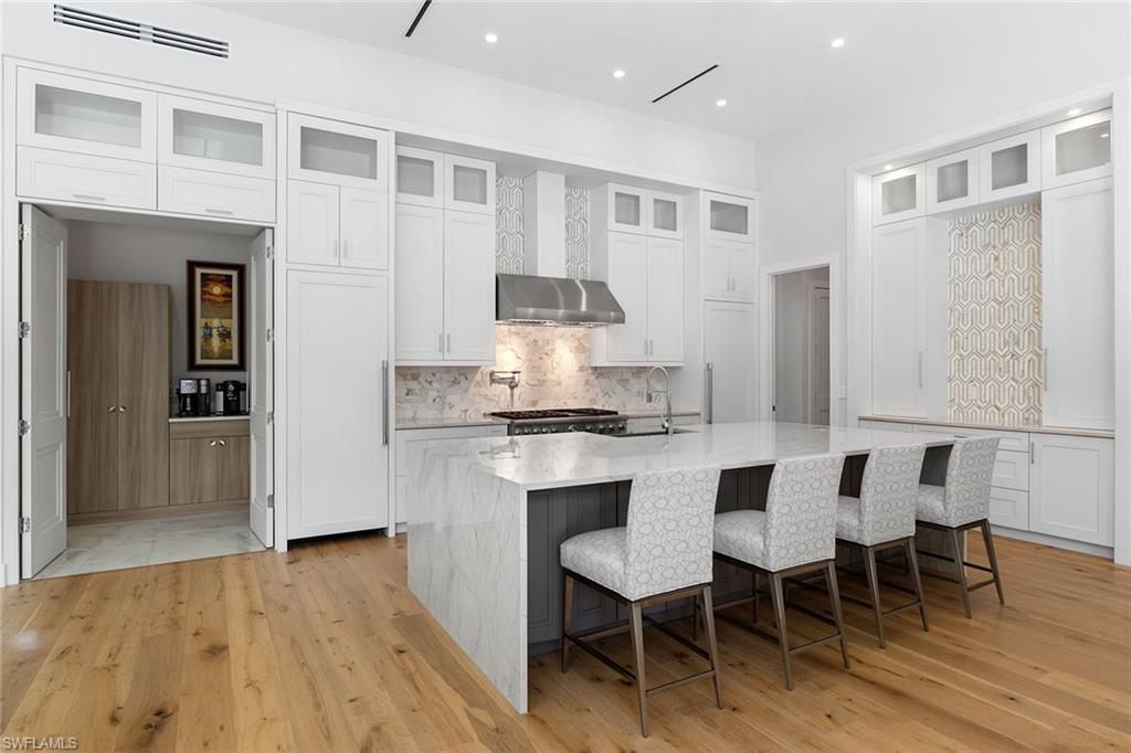720 Orchid Drive Naples, FL 34102 - Photo 16 of 50 a kitchen with stainless steel appliances granite countertop a stove top oven a refrigerator a dining table and chairs with wooden floor