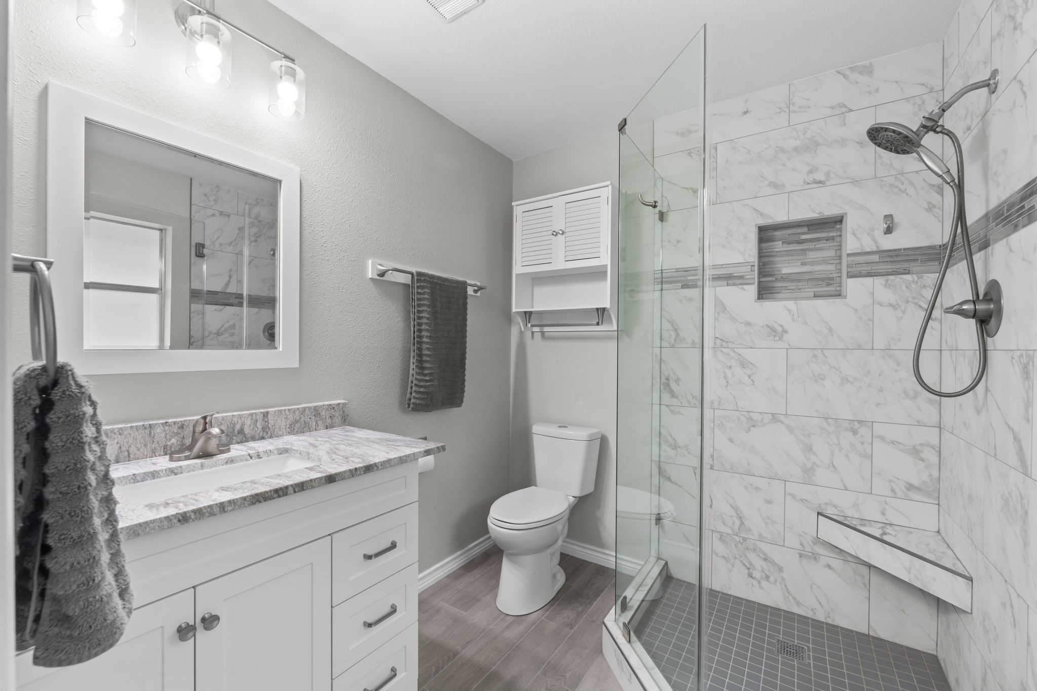 209 Summit Drive Conroe, TX 77303 - Photo 6 of 22 The fully renovated primary bathroom features a spacious tiled shower with a built-in corner bench, updated light fixtures, vanity, granite counter top, sink, new LVP flooring, new trim, and elegant finishes throughout.