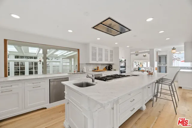 a kitchen with stainless steel appliances a stove a sink a refrigerator and white cabinets with wooden floor