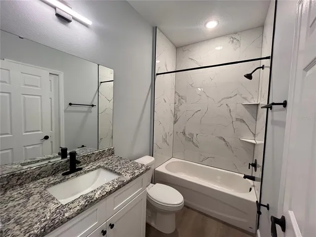 a bathroom with a granite countertop sink toilet mirror and bathtub