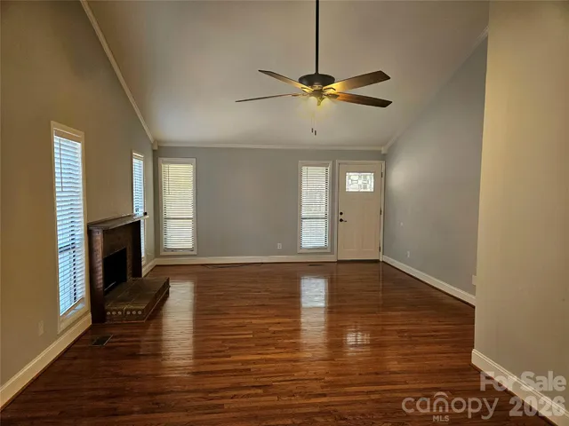 a view of an empty room with wooden floor fireplace and a window