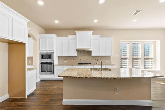 a large kitchen with granite countertop a stove a sink a refrigerator and white cabinets with wooden floor