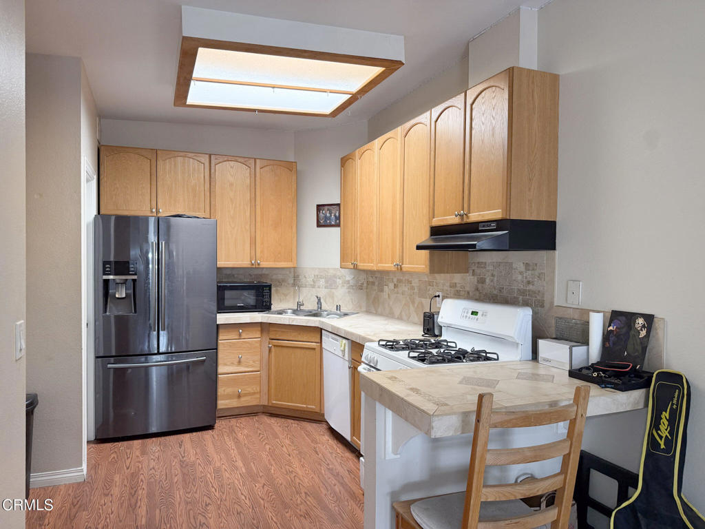 3000 Isle Way, Unit C Oxnard, CA 93035 - Photo 6 of 22 a kitchen with a refrigerator a stove a sink and white cabinets with wooden floor