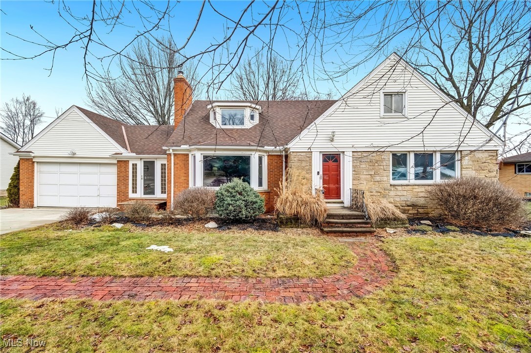 View of front of property featuring an attached garage, driveway, stone siding, a front lawn, and a chimney