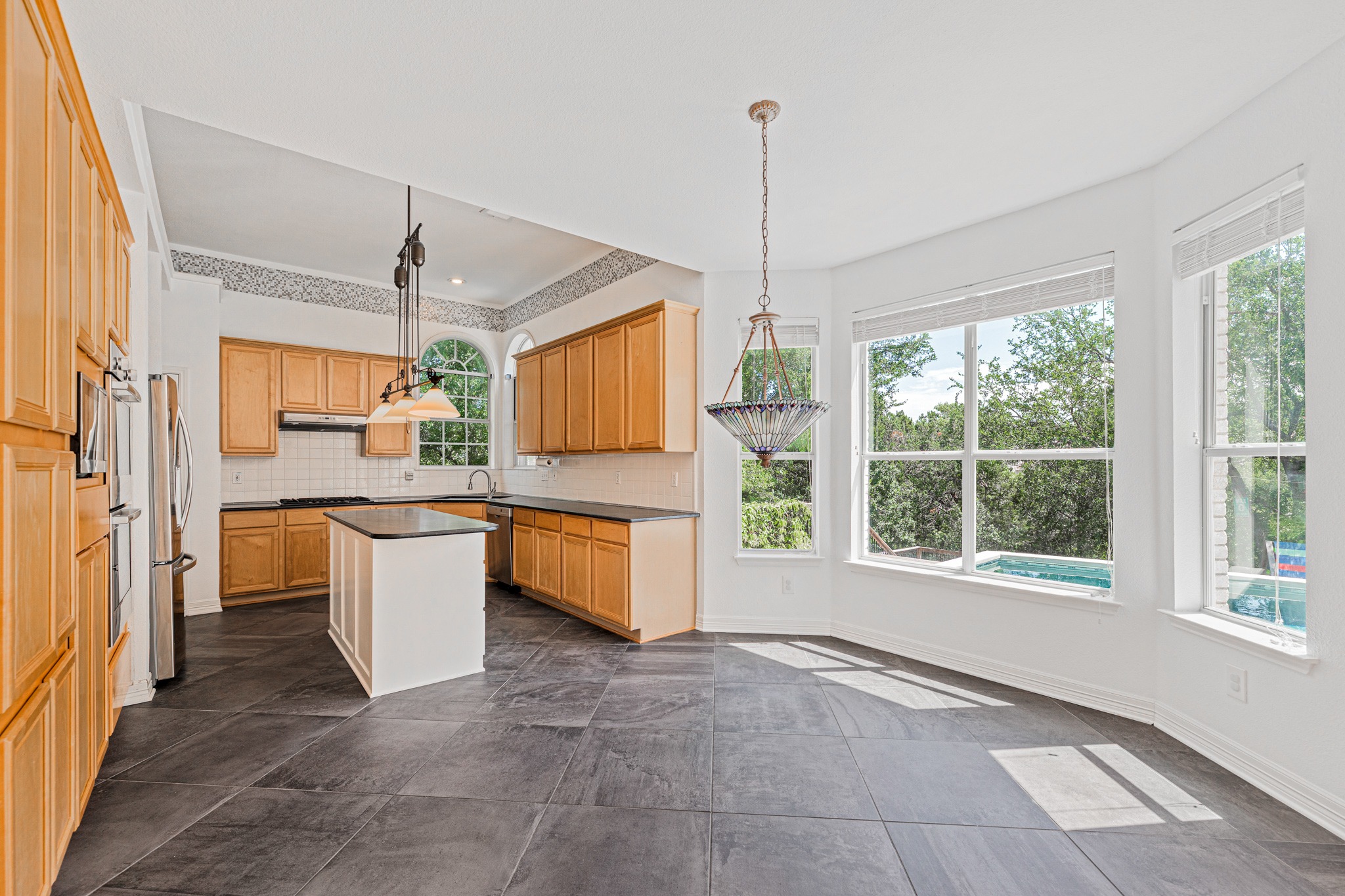 304 River Down Road Georgetown, TX 78628 - Photo 6 of 22 Kitchen and dining area featuring dark tile flooring, light wood cabinetry, a central island, and multiple windows
