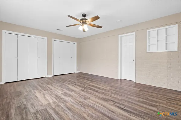 a view of an empty room with wooden floor and a ceiling fan