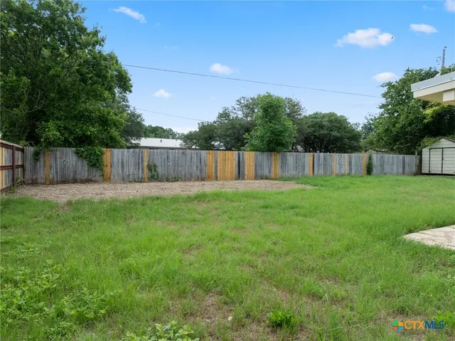 a swimming pool that is in the grass with large trees and wooden fence
