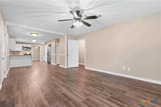 a view of an empty room with wooden floor and a ceiling fan