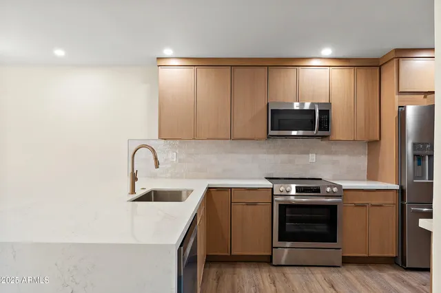 a kitchen with stainless steel appliances a sink a stove a microwave a refrigerator a sink and cabinets