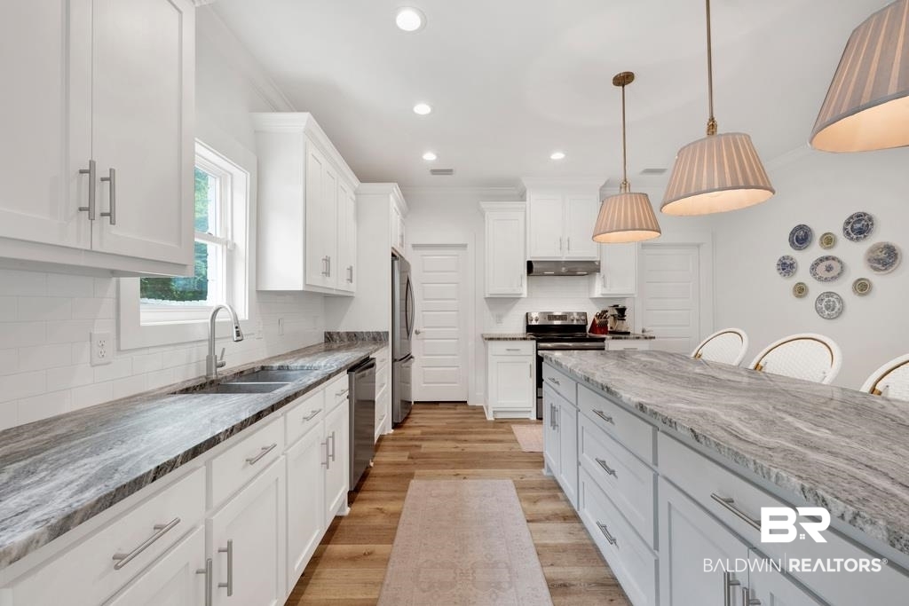 379 Pecan Ridge Boulevard Fairhope, AL 36532 - Photo 6 of 21 Kitchen featuring an expansive island with a light-toned, veined countertop, white cabinetry with brushed nickel hardware, wood-finish flooring, recessed lighting, and a subway tile backsplash