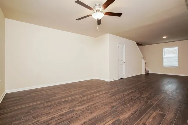 an empty room with wooden floor fan and windows