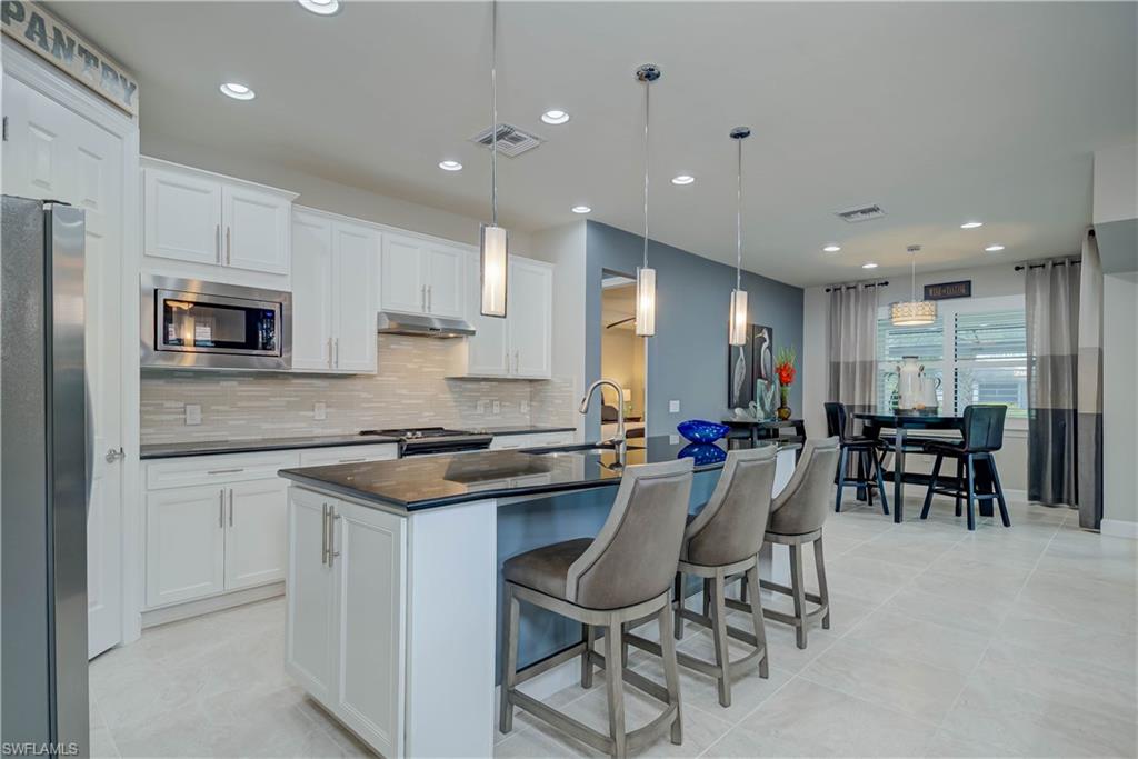 7938 Guadiana Way Ave Maria, FL 34142 - Photo 10 of 37 a kitchen with stainless steel appliances kitchen island granite countertop a stove a refrigerator a white table a sink and chairs
