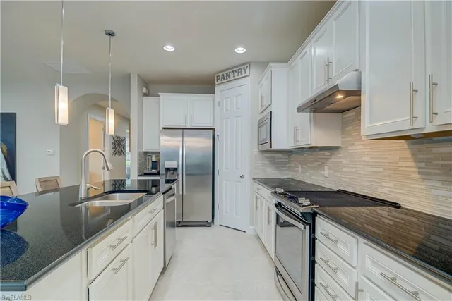 a kitchen with stainless steel appliances kitchen island granite countertop a stove a refrigerator a white table a sink and chairs