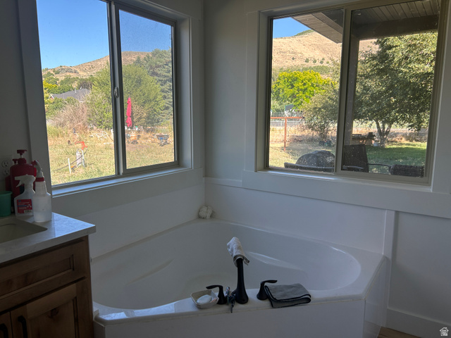2688 Read Lane Preston, ID 83263 - Photo 11 of 18 Corner soaking tub with matte black fixtures, quartz vanity countertop, wood-finish cabinetry, and expansive window views of surrounding hills and mature trees