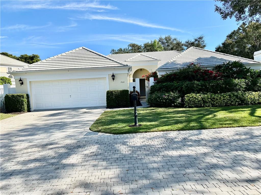 7010 Rue De Marquis Naples, FL 34108 - Photo 2 of 8 Ranch-style house featuring a tiled roof, decorative driveway, a front lawn, an attached garage, and stucco siding