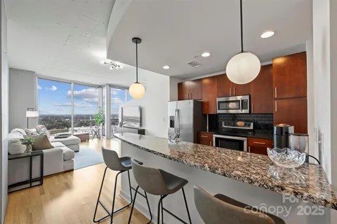 a kitchen with stainless steel appliances granite countertop a stove a sink and a living room view